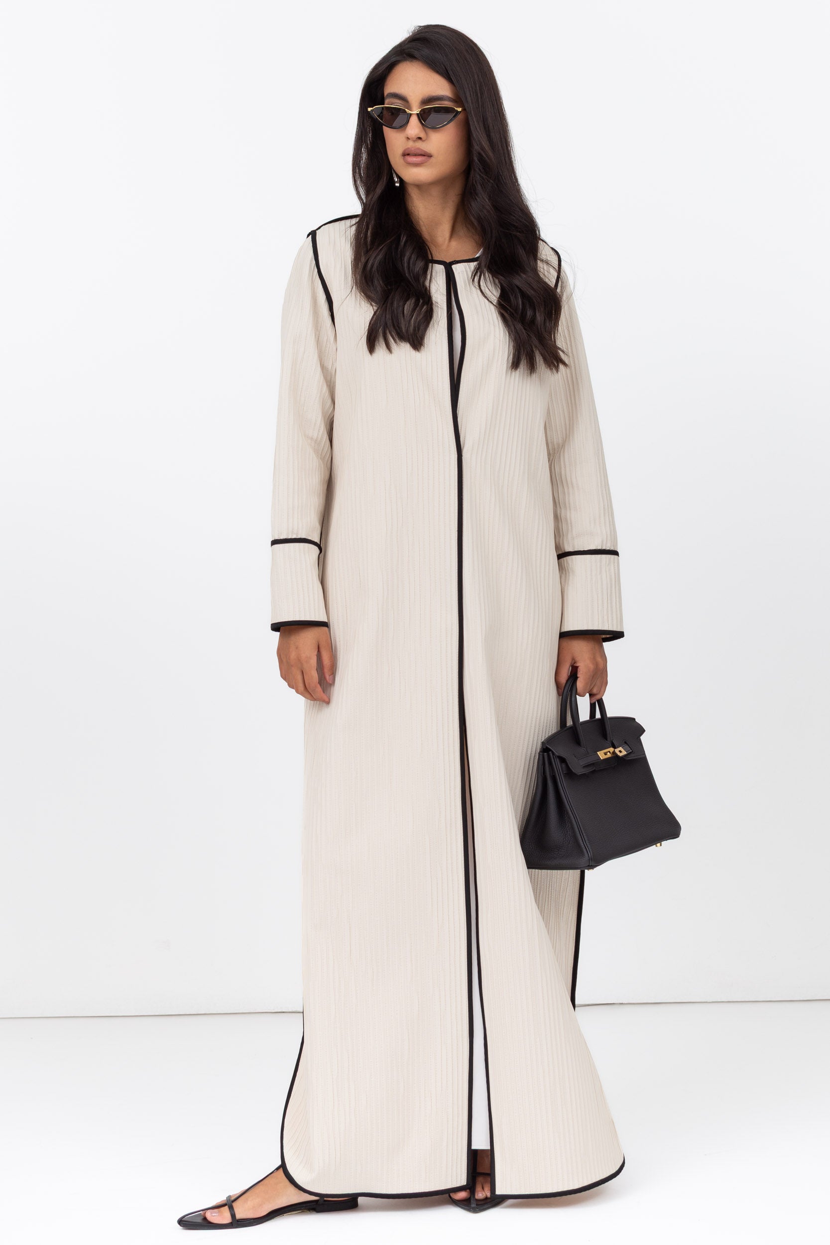 Woman wearing a long cream coat with black trim on a white background