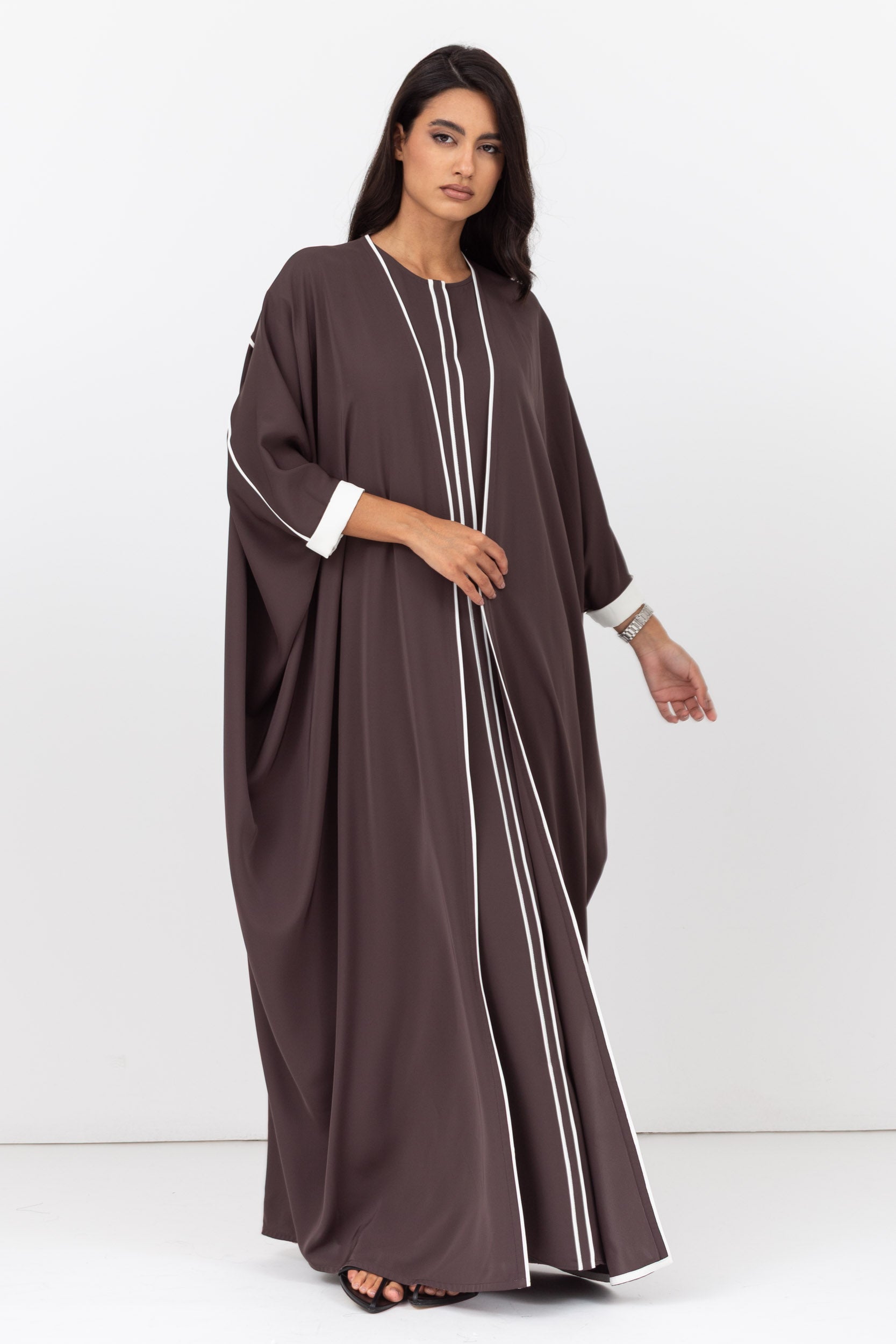 Woman wearing a brown abaya with white trim on a white background