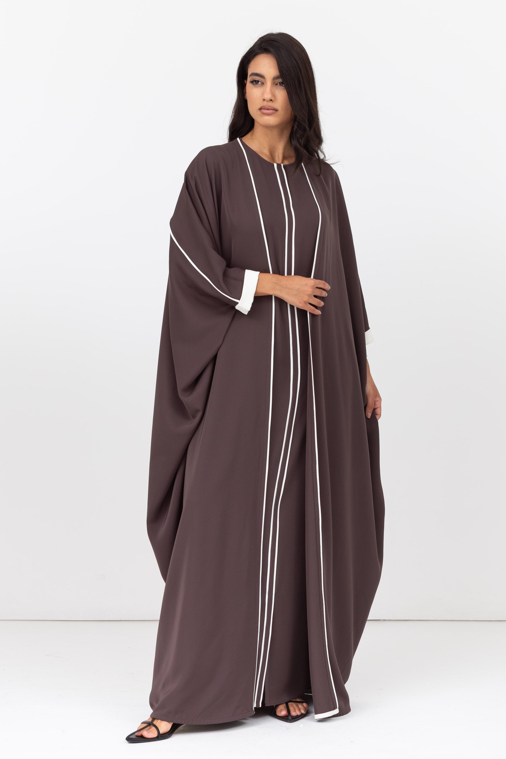 Woman wearing a long brown dress with white trim on a white background